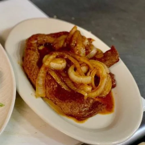 Bistec Encebollado - Steak with sautéed onions, served with rice and beans.